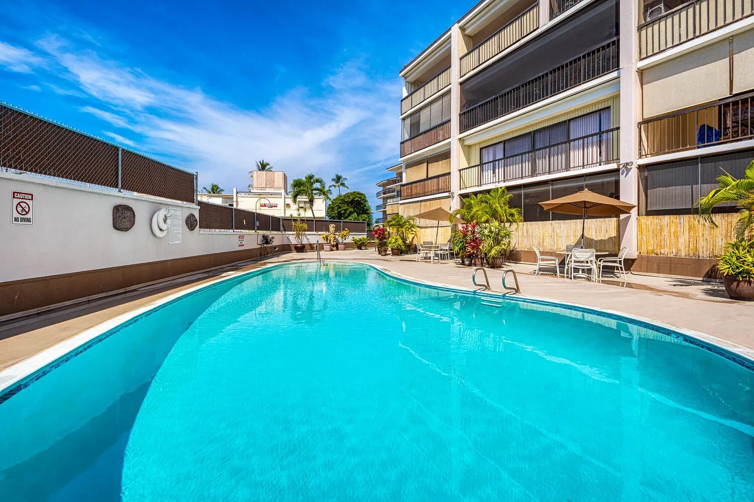 Una piscina al aire libre junto a un edificio de varios pisos y una zona de estar.