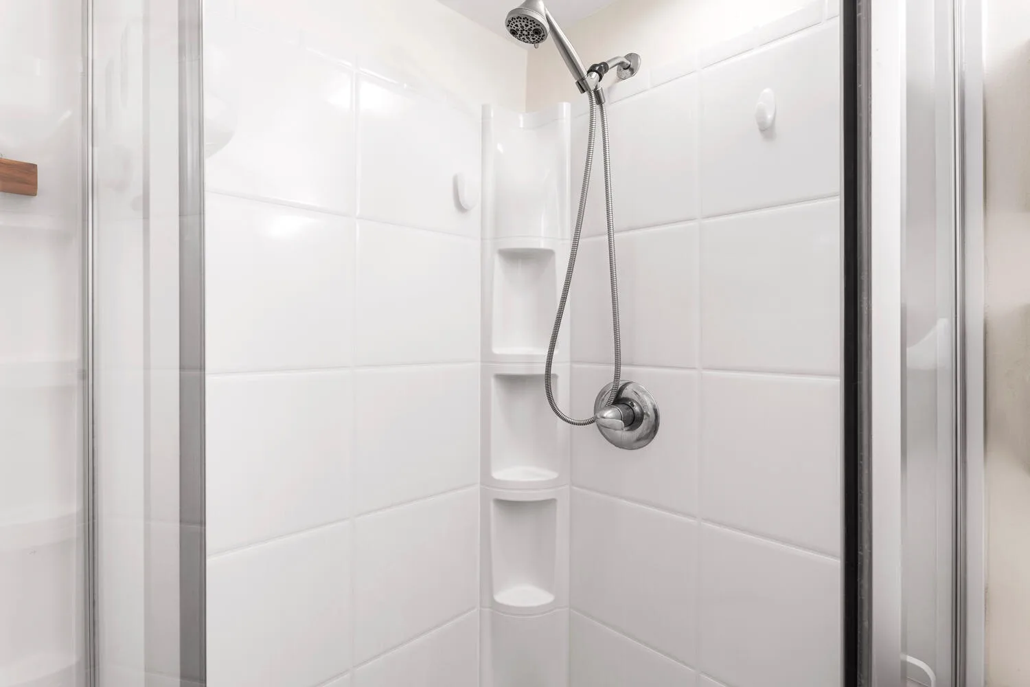 Una ducha con azulejos, ducha de mano y estantes en la esquina.