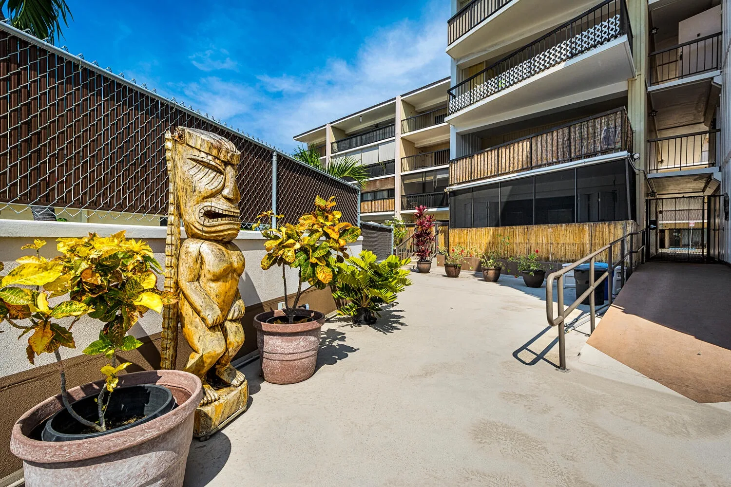 Un pasillo de patio exterior con plantas en macetas junto a un edificio de varios pisos.
