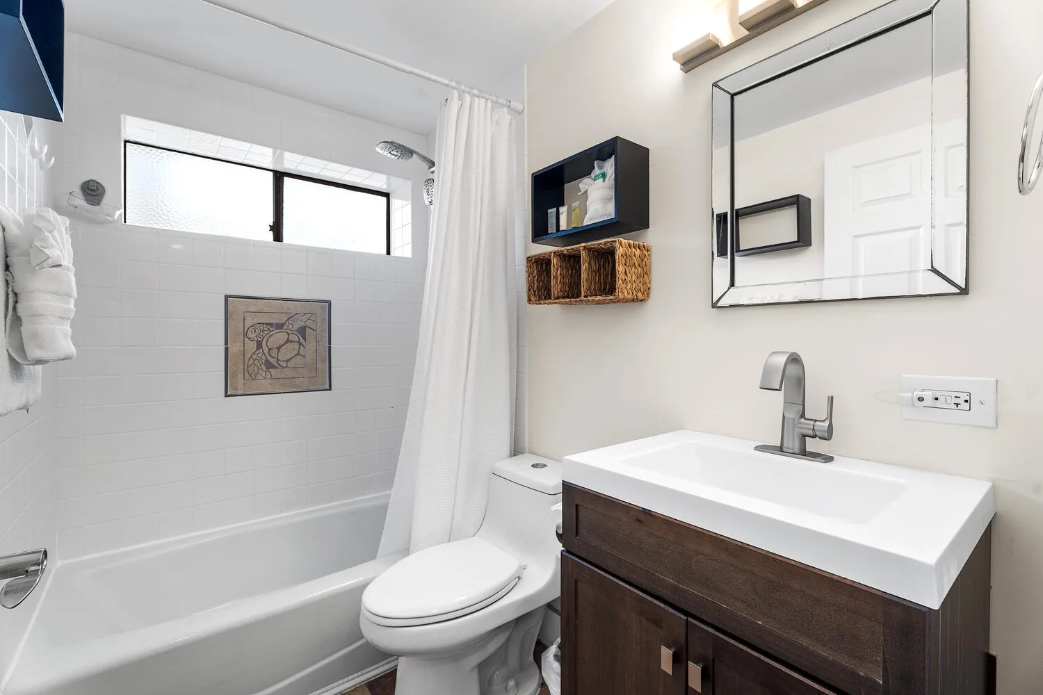 Un baño luminoso con bañera, cortina de ducha, inodoro y lavabo con mueble.