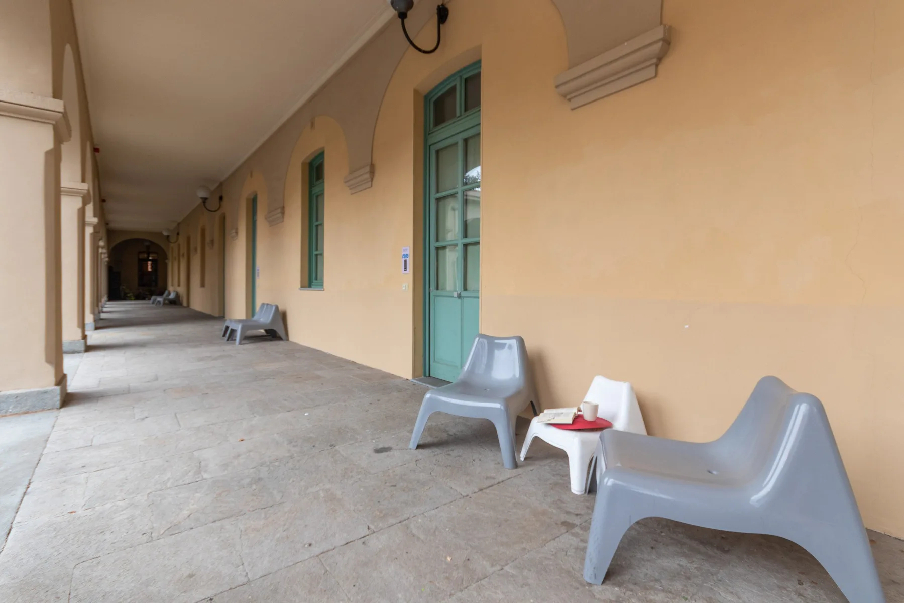 Un pasillo exterior cubierto con puertas turquesas y asientos junto a la pared.