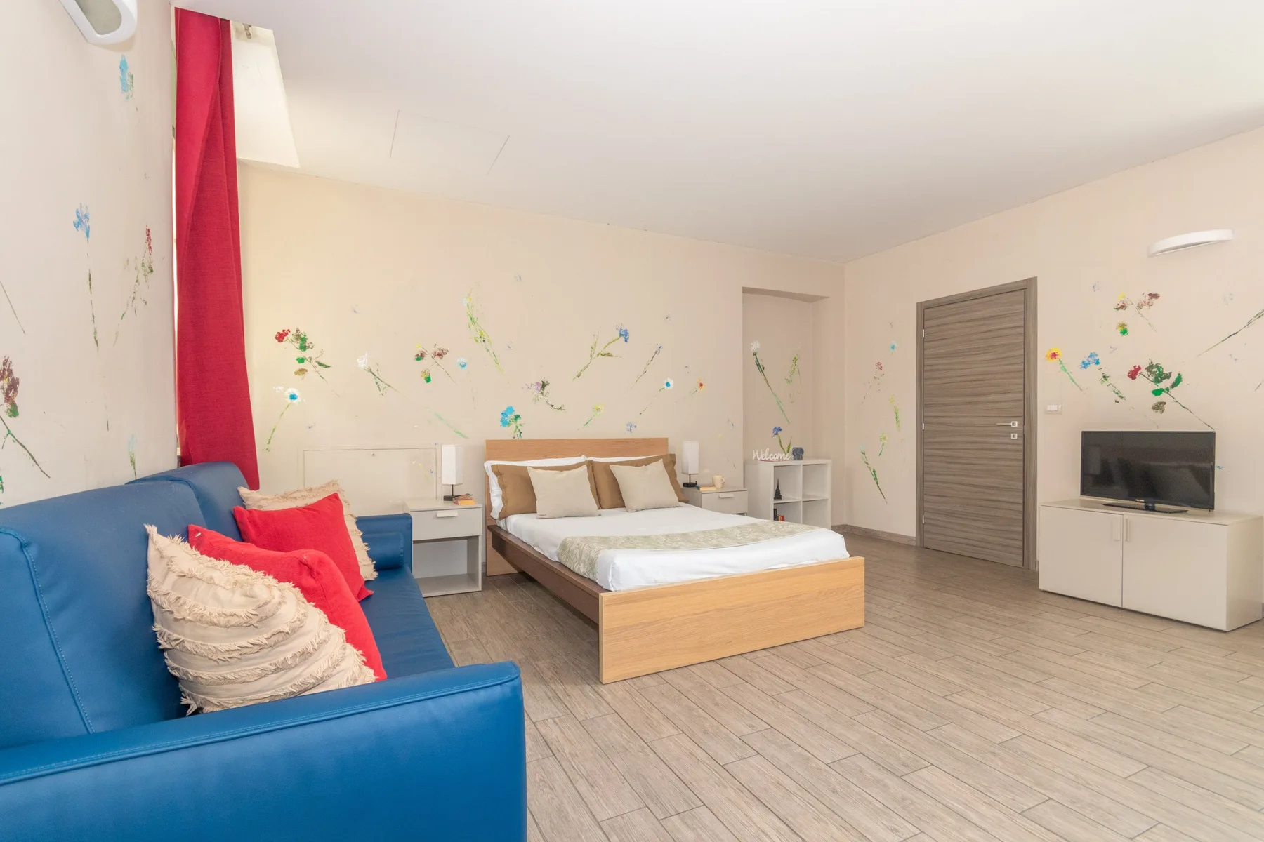 Un dormitorio con una cama, asientos azules y un televisor junto a la pared.