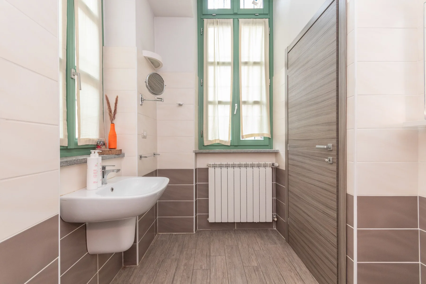 Un baño con lavabo de pared, radiador y ventana.