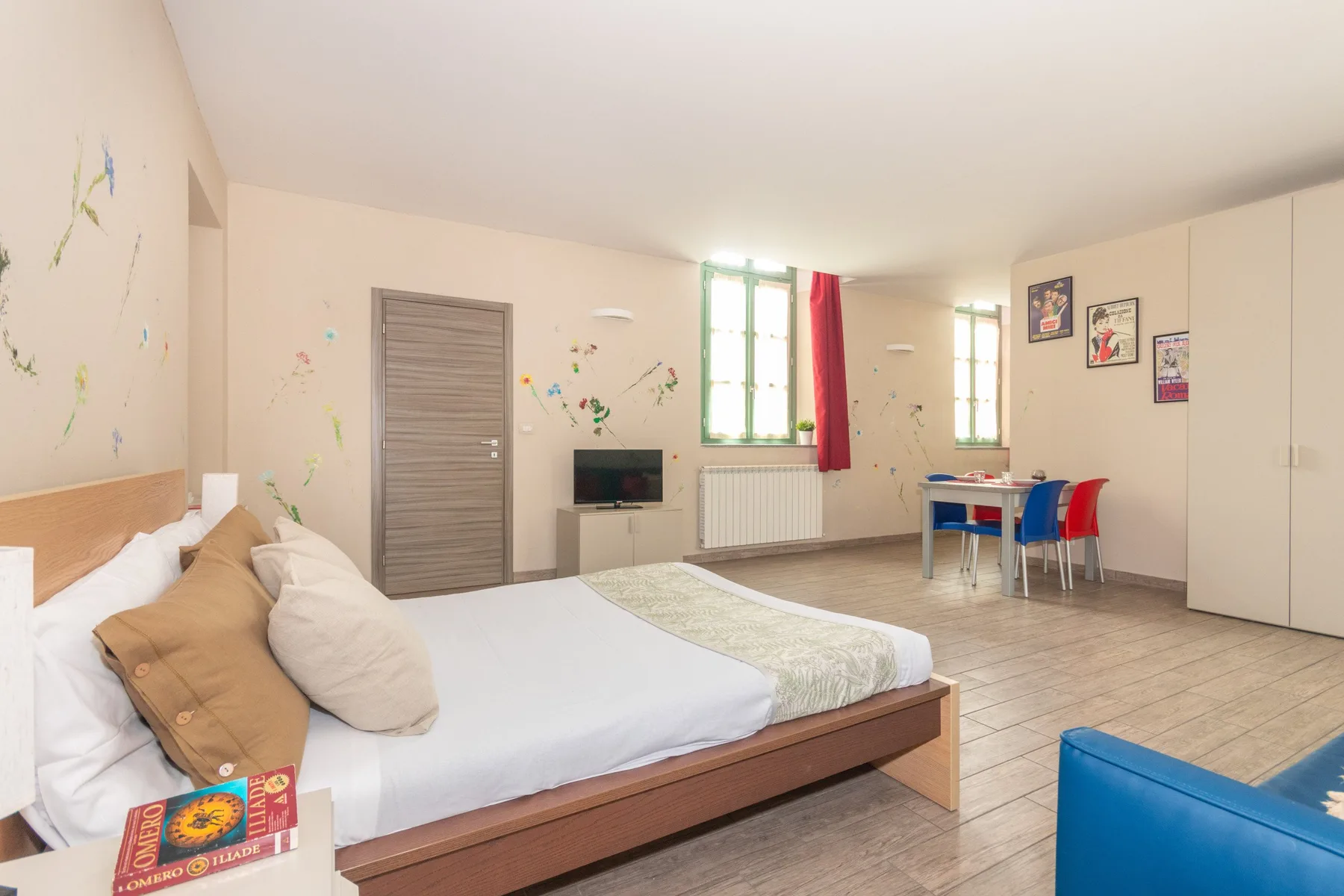 Un dormitorio con una cama grande, ventanas y una pequeña mesa de comedor.