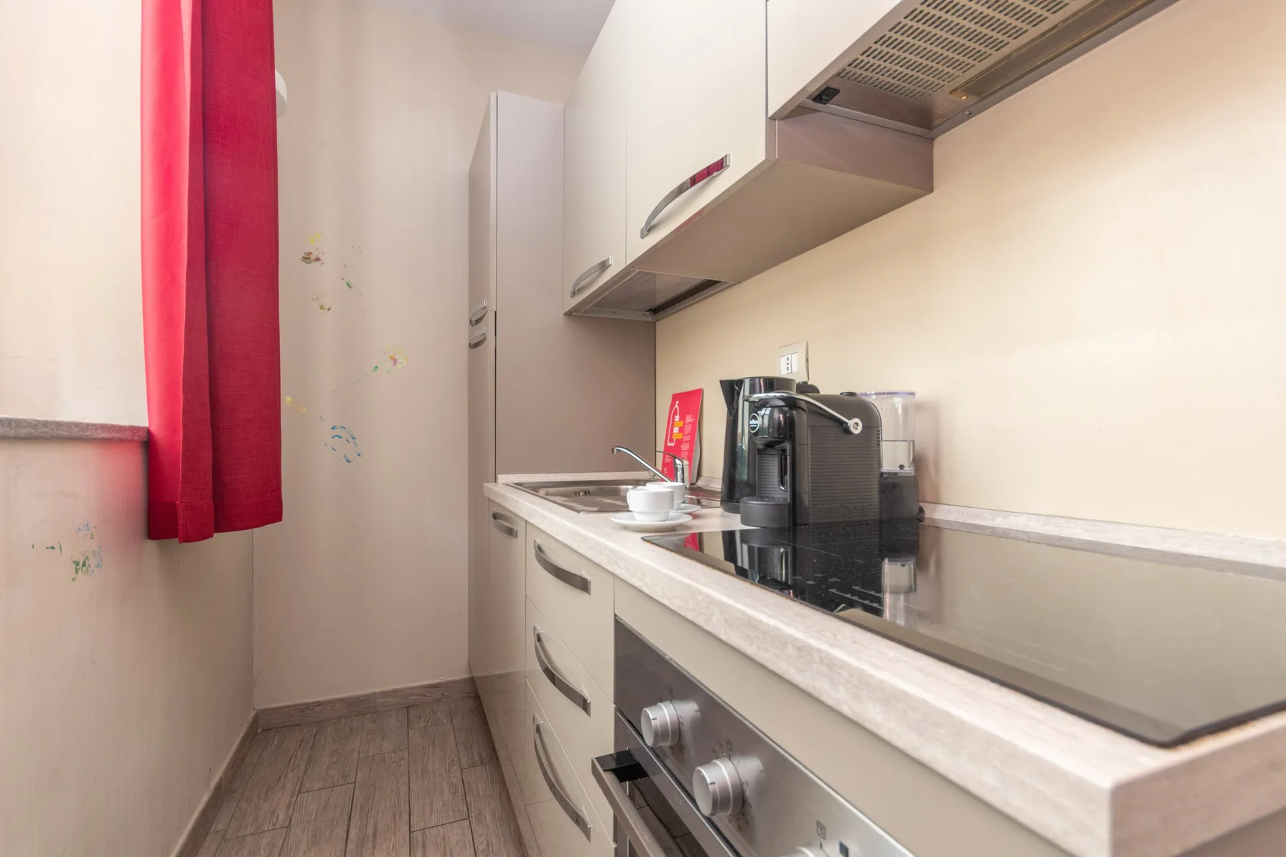 Una cocina estrecha con una cafetera sobre la encimera y una cortina roja.