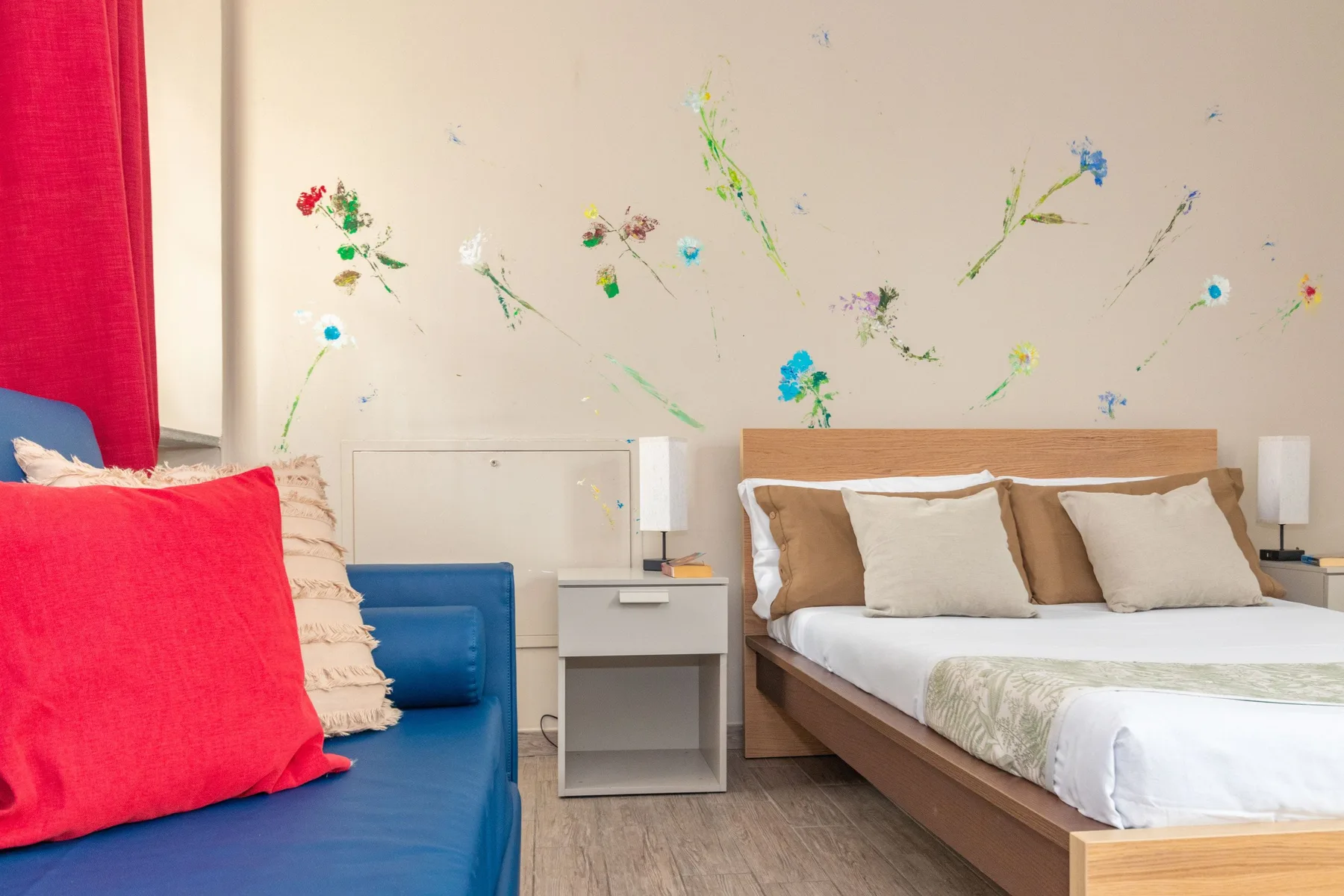 Un dormitorio con una cama doble, una mesita de noche y adornos florales coloridos en la pared.