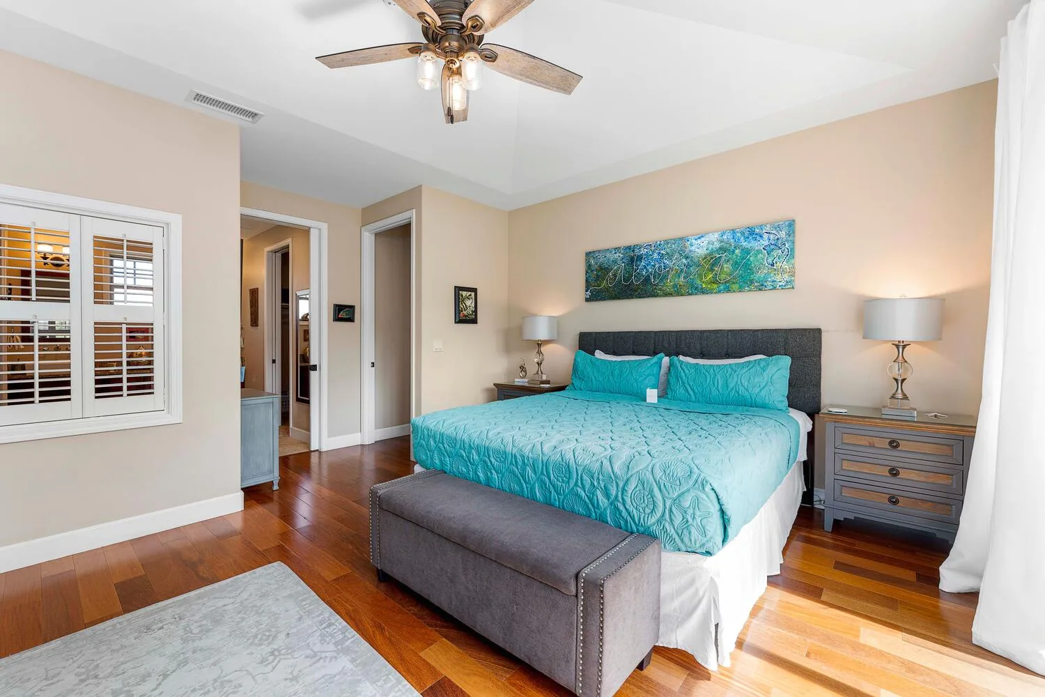 A bedroom with a turquoise bed, matching pillows, and a gray upholstered bench.