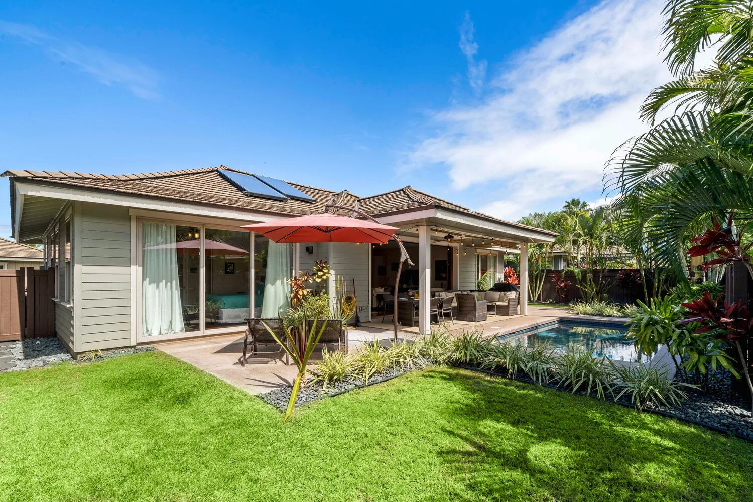 A single-story house opens onto a patio beside a swimming pool and lawn.