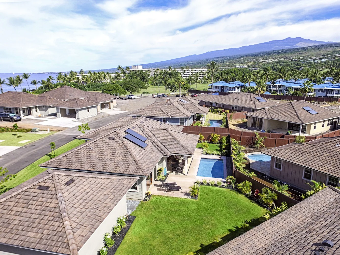 Aerial view of homes with tiled roofs, green lawns, and a small swimming pool.