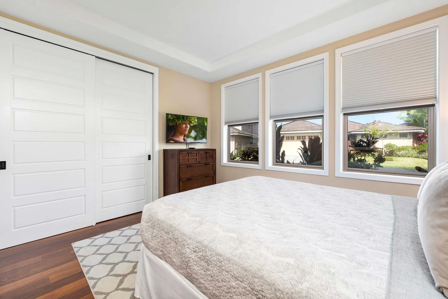 A bright bedroom with a large bed, white closet doors, and windows overlooking greenery.
