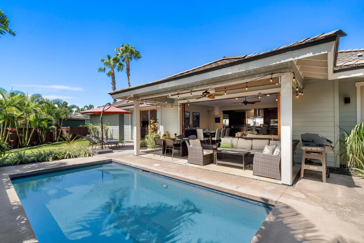 A swimming pool in front of a covered outdoor seating area beside a house.