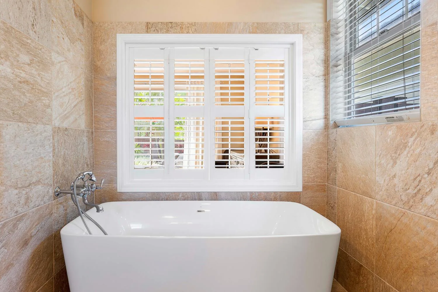 A bathroom with a freestanding bathtub and shuttered windows.