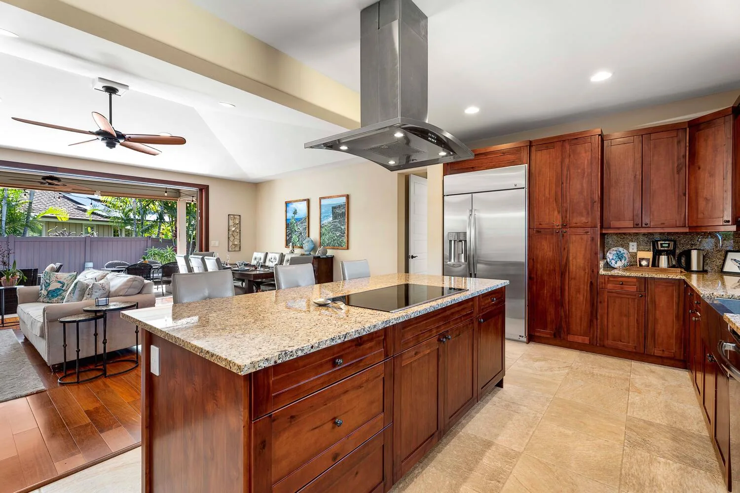 An open-plan kitchen with a stone island and wooden cabinets beside a living area.
