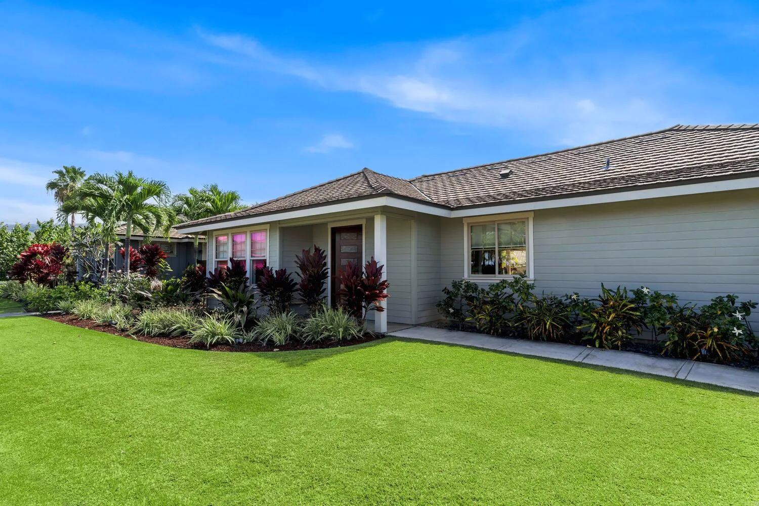 A single-story house with a tiled roof stands behind a broad green lawn.