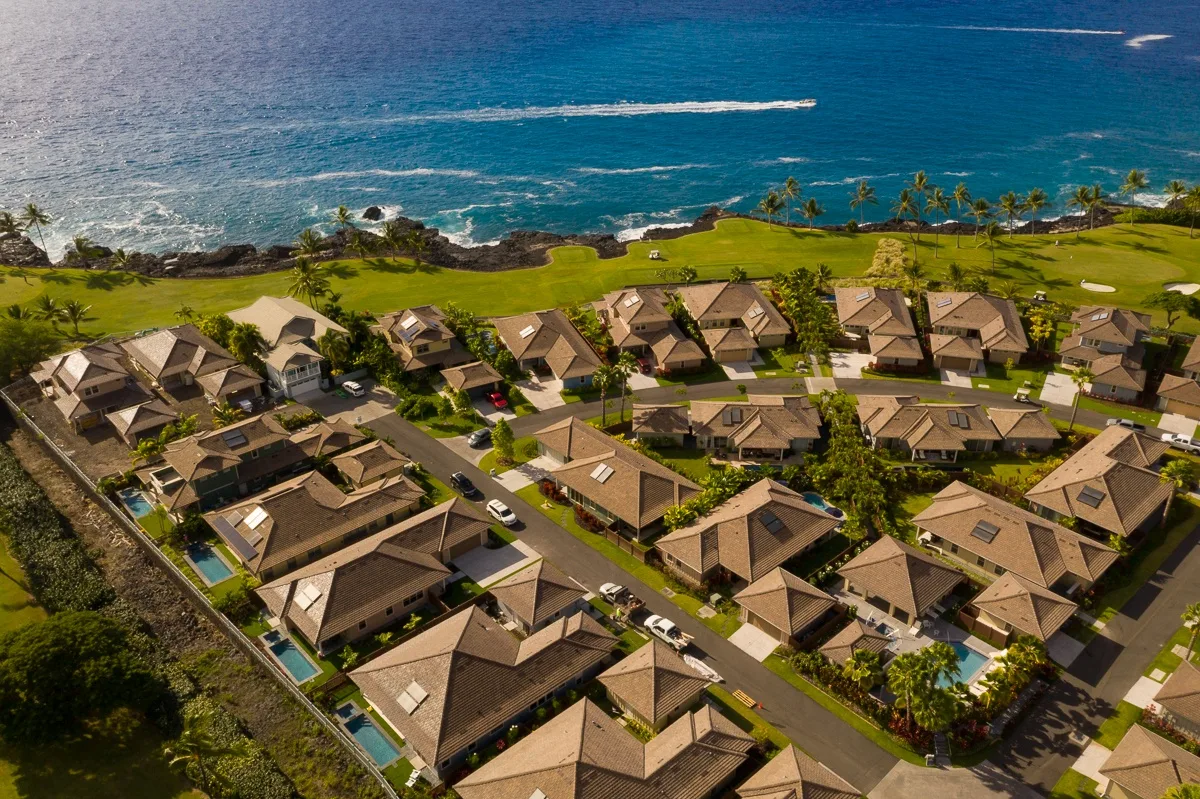 An aerial view of homes beside a green lawn and the ocean.