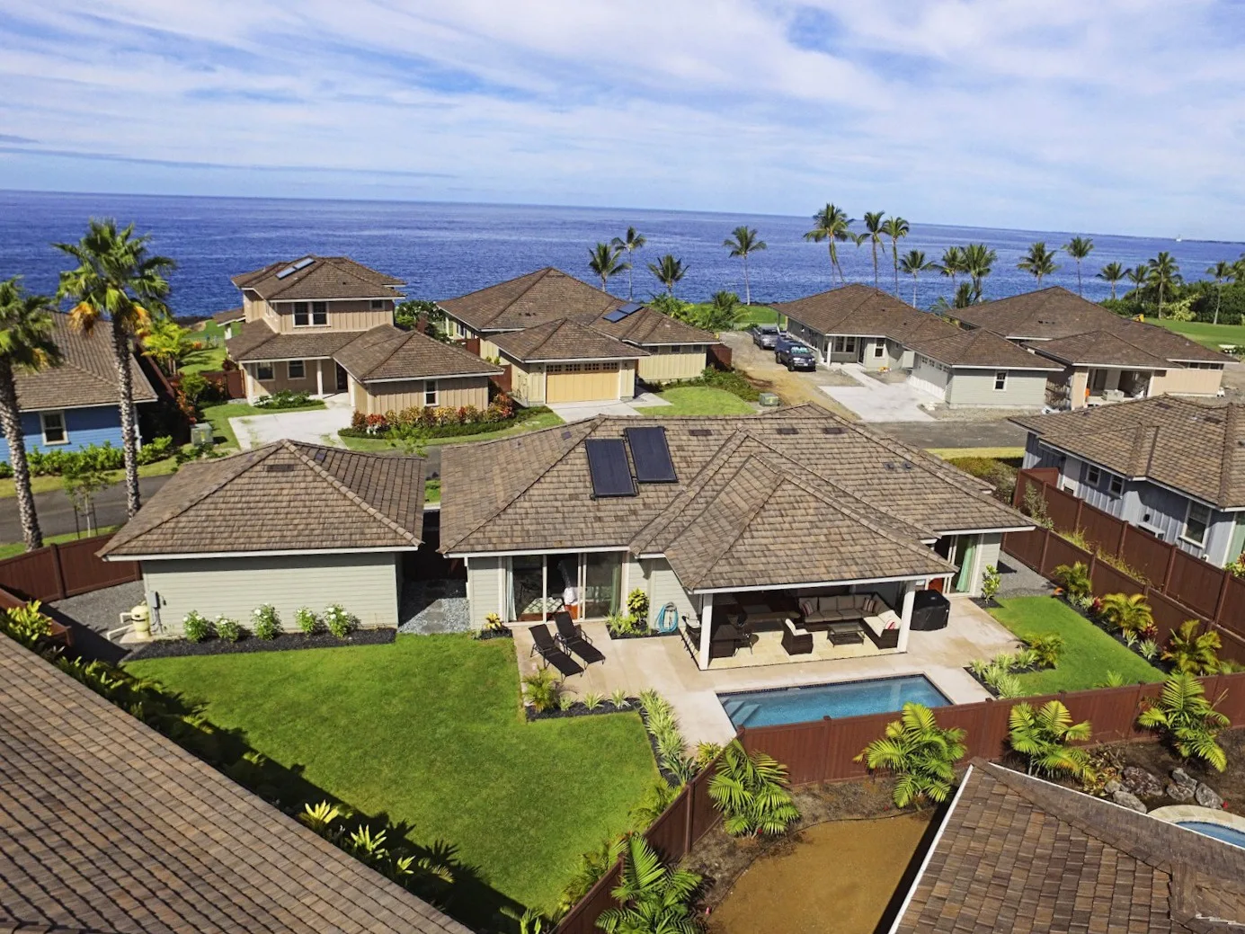 Aerial view of homes with tiled roofs, green lawns, and the ocean beyond.