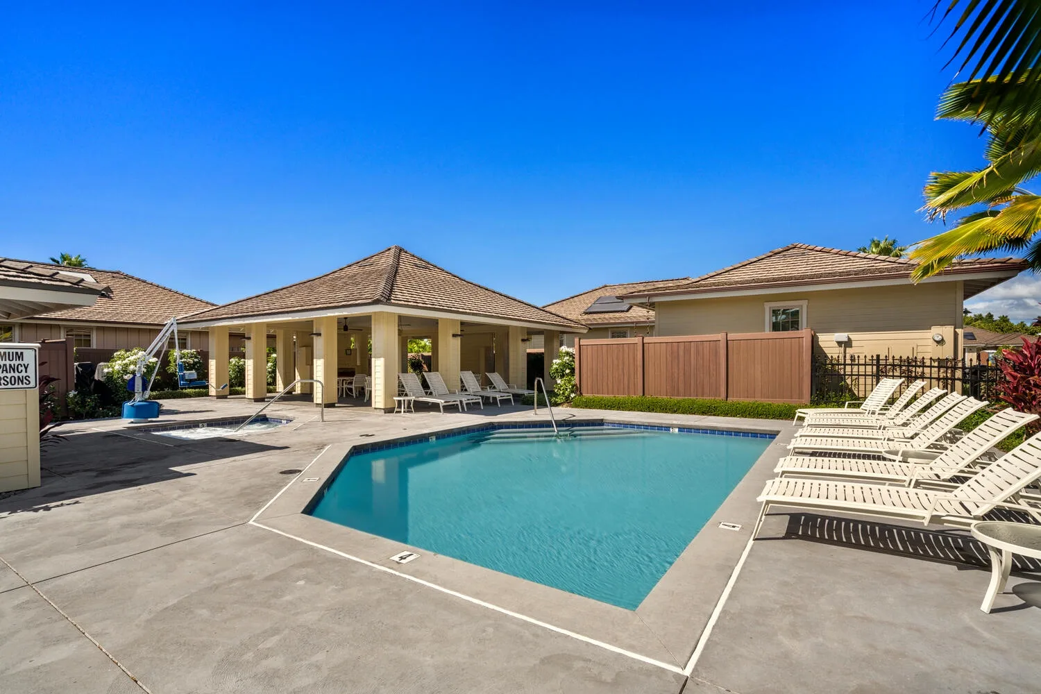 An outdoor swimming pool is surrounded by lounge chairs and low buildings.