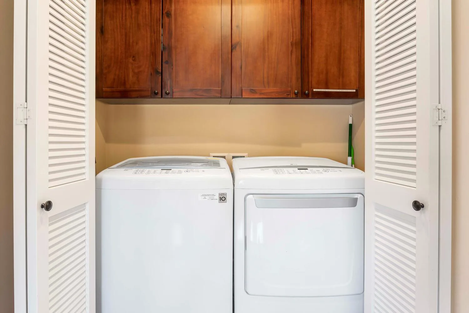 Laundry area with a washer and dryer beneath wooden cabinets.