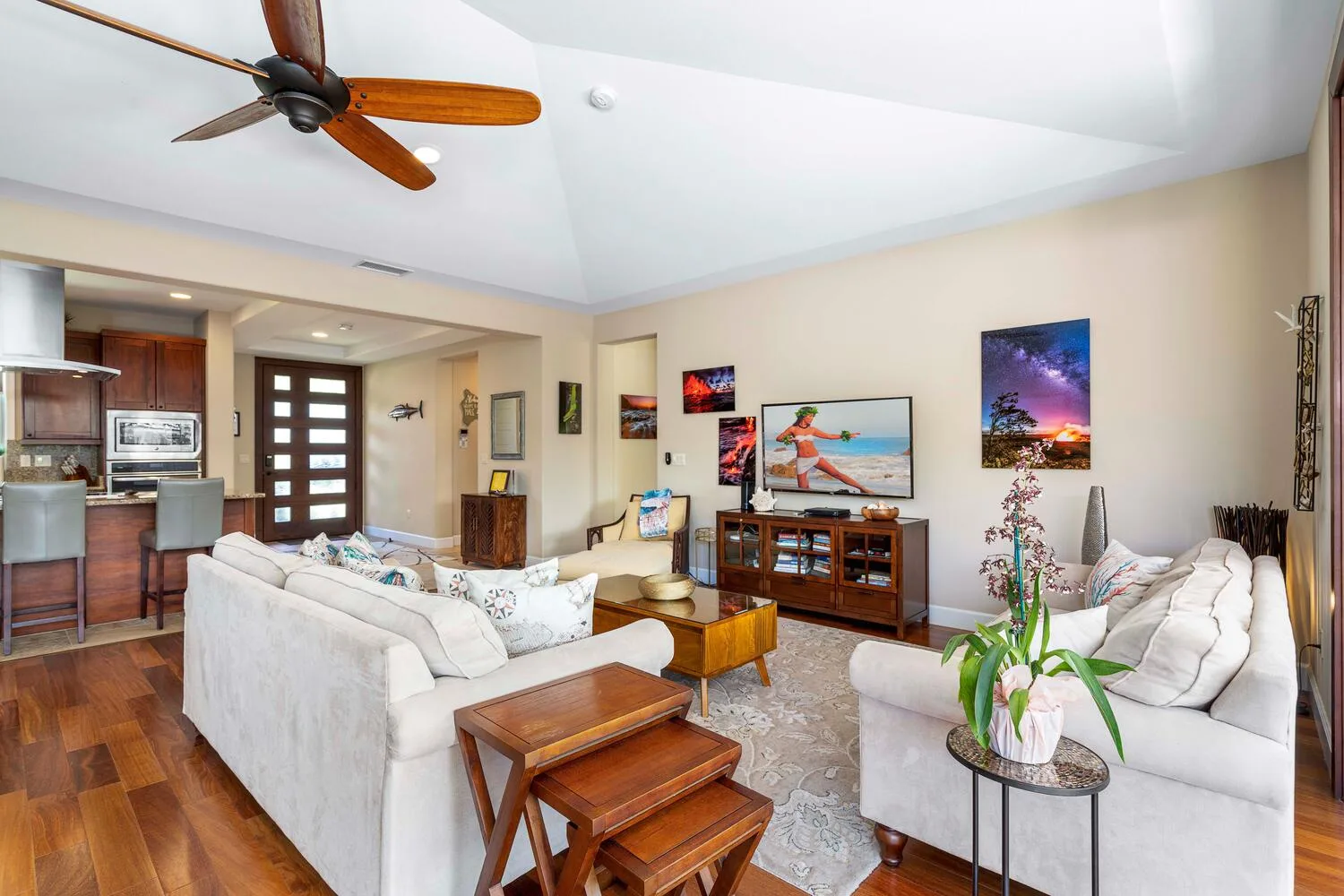 A living room with light-colored seating, a television, and an open kitchen.