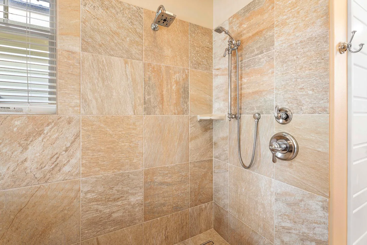 A tiled shower with a handheld showerhead and window.