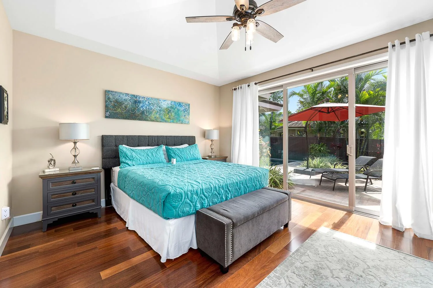 A bedroom with a turquoise bed and sliding glass doors opening onto a patio.
