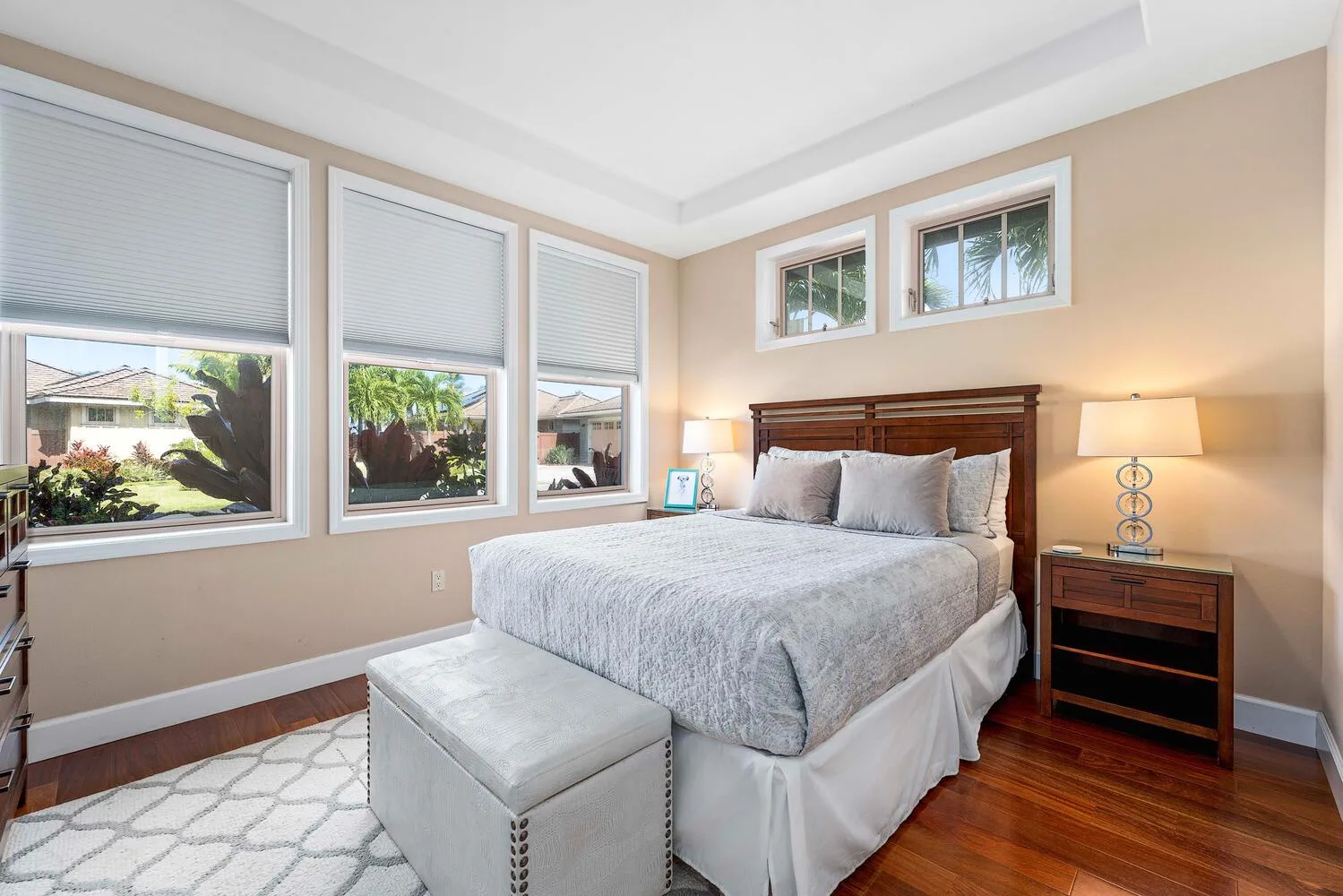 A bright bedroom with a large bed, bedside tables, and windows overlooking greenery.