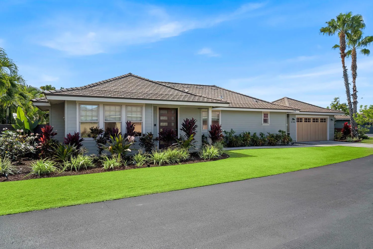 A single-story house with a garage stands behind a lawn and landscaped garden.