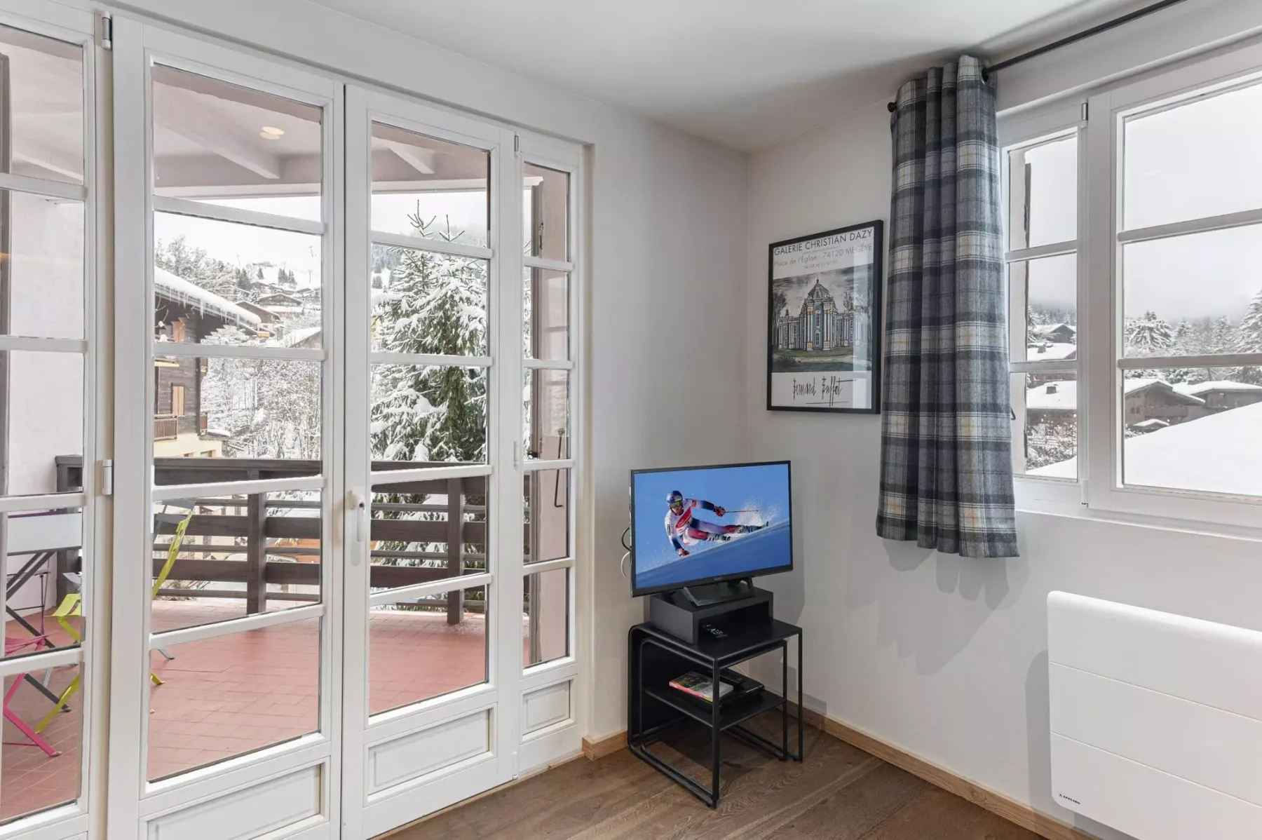 Una luminosa zona de estar con televisor y ventanas con vistas a un paisaje nevado.