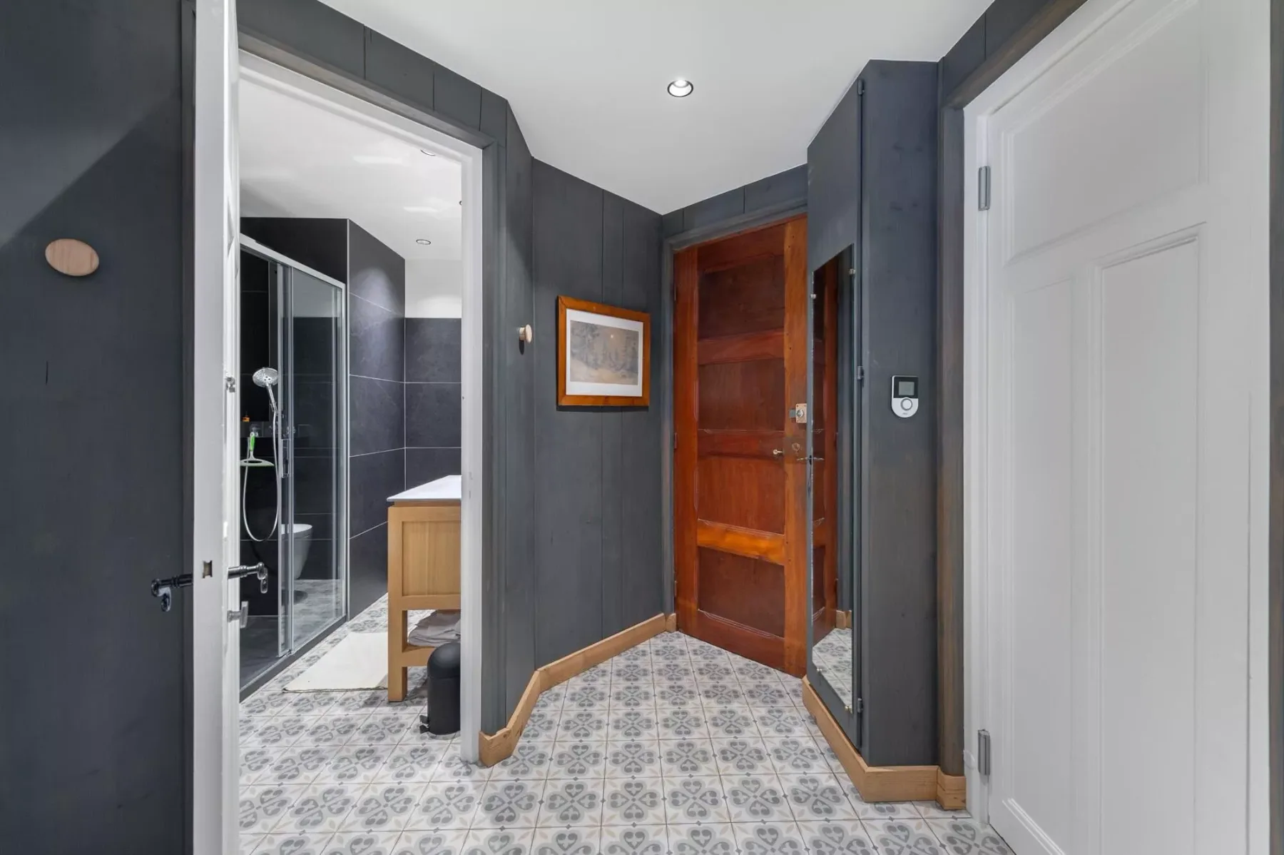 Un pasillo interior con suelo de baldosas estampadas y una puerta de madera.