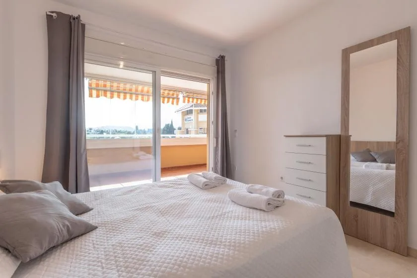 A bright bedroom with a bed beside sliding glass doors opening onto a balcony.