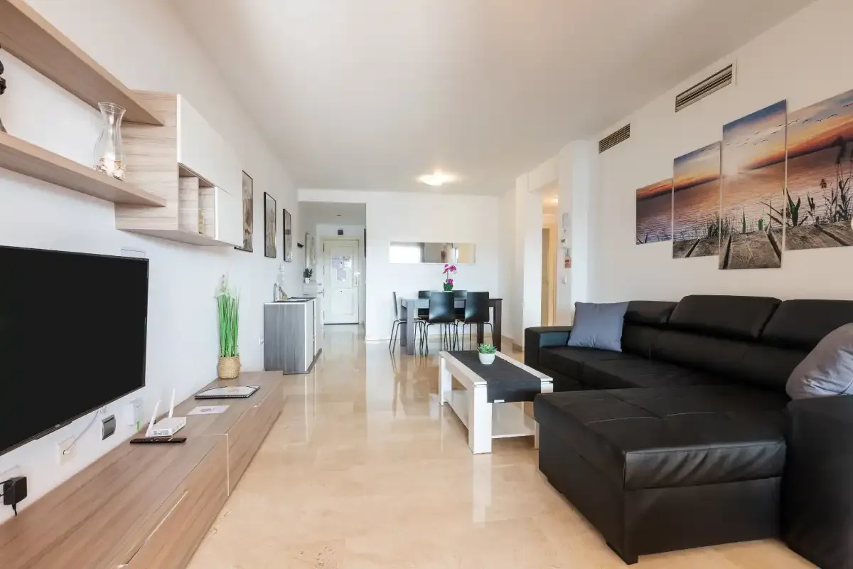 A bright living room has dark seating, a television, and a dining table.