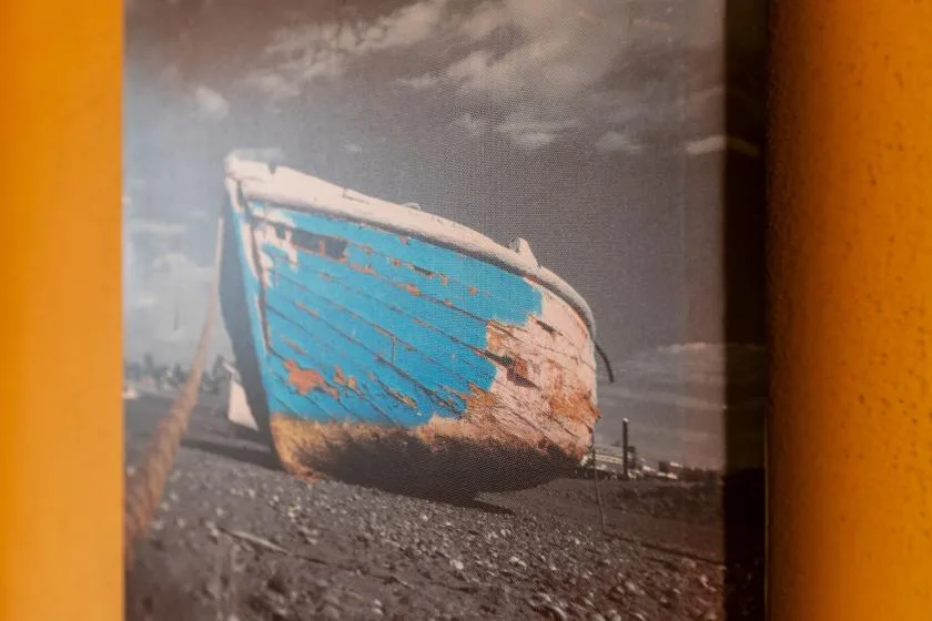 A framed photograph shows a weathered blue boat resting on a shore.