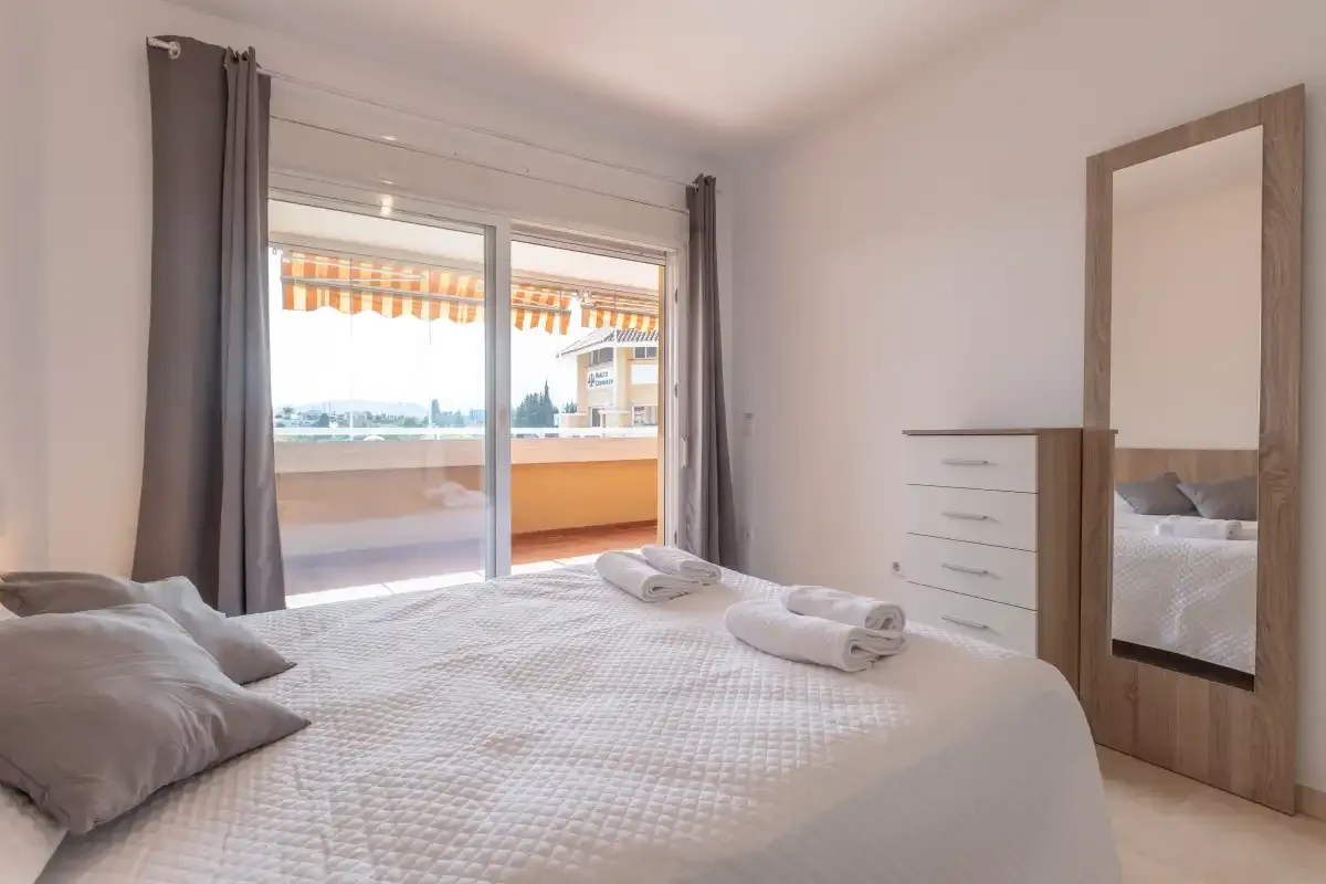 A bedroom with a bed, dresser, and sliding glass doors opening onto a balcony.