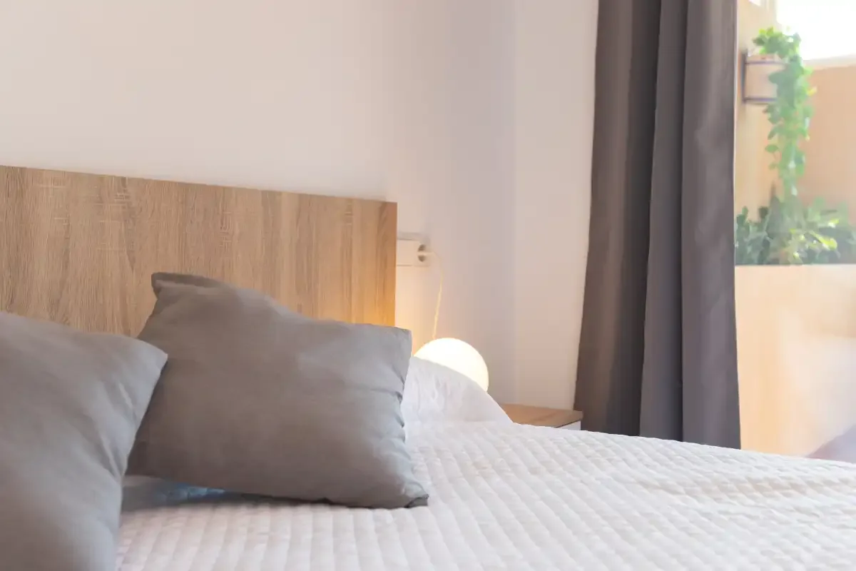 A bedroom with a bed, wooden headboard, and a window beside dark curtains.