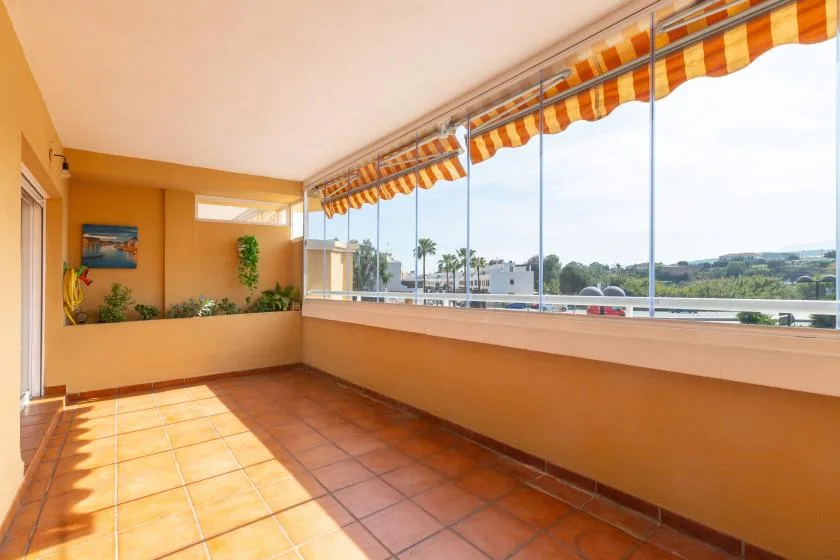 A sunlit enclosed balcony with tiled flooring and large windows overlooking the landscape.