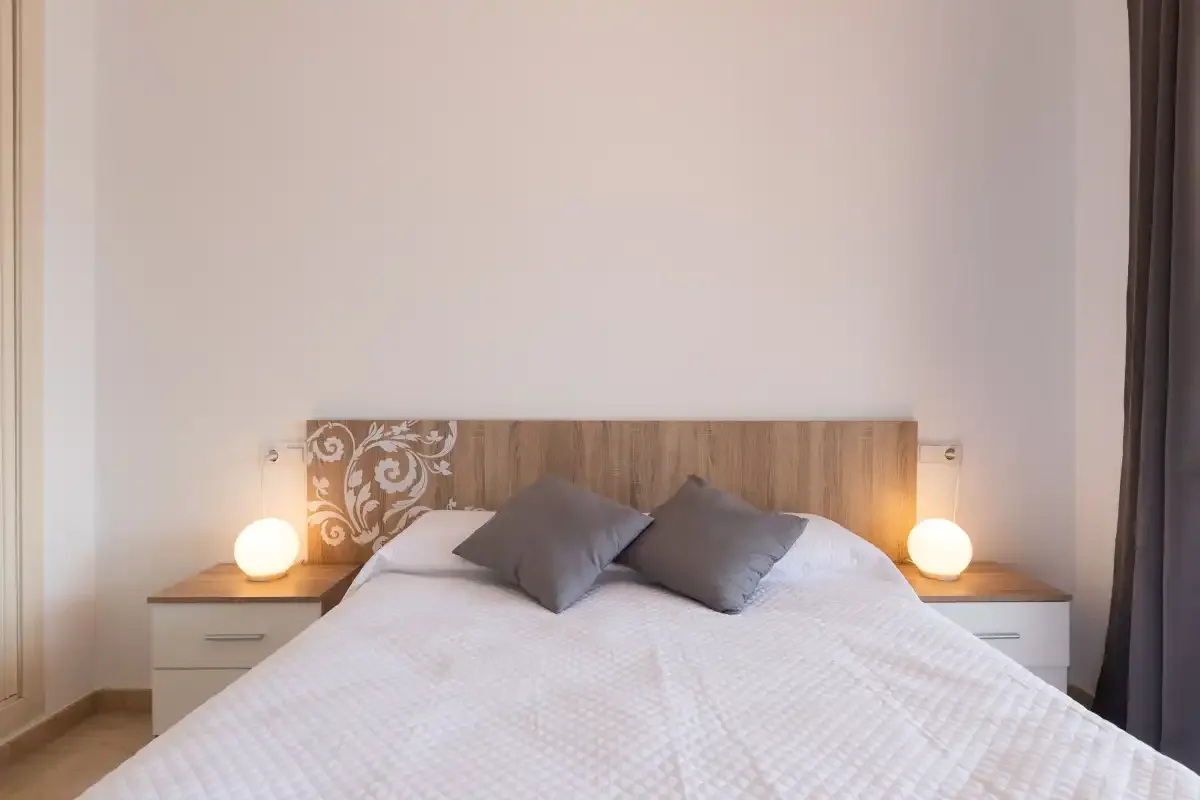 A bedroom with a bed, two pillows, and matching bedside lamps.