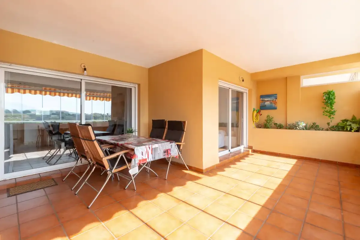 A sunny tiled terrace with a dining table, chairs, and potted plants.