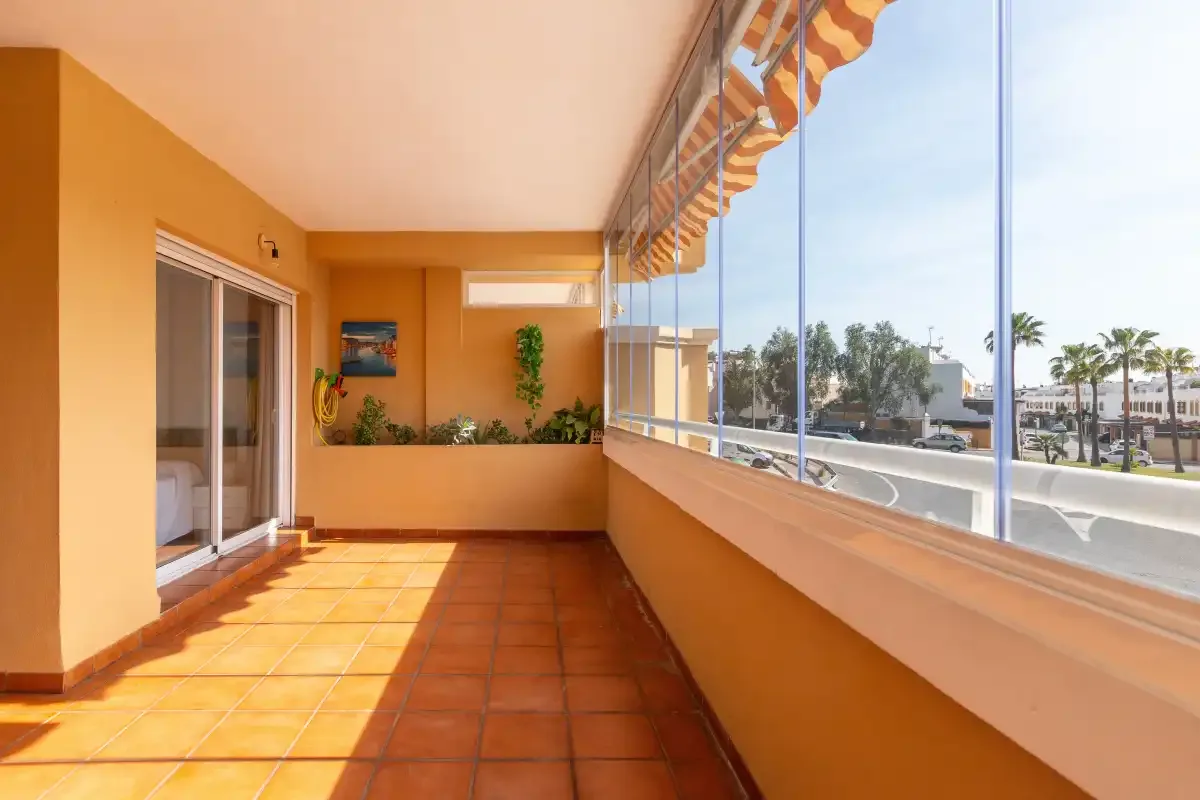 A sunny enclosed balcony with terracotta-colored floor tiles and large windows.