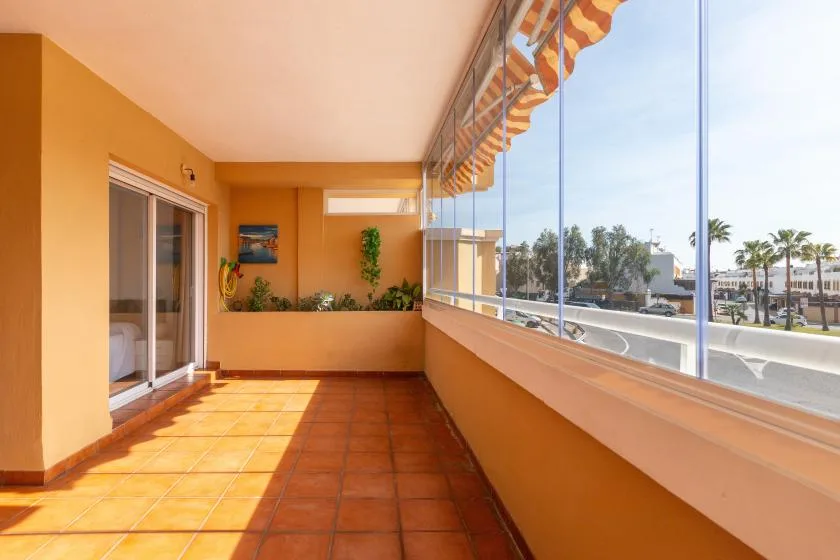 A sunlit balcony with terracotta tiles and a glass railing.