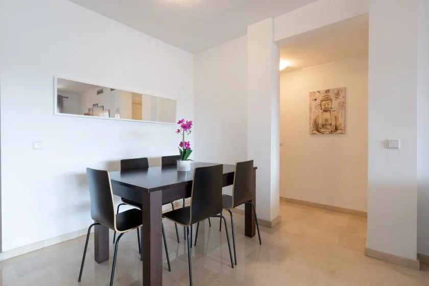 A dining area with a dark table and chairs beside an open hallway.