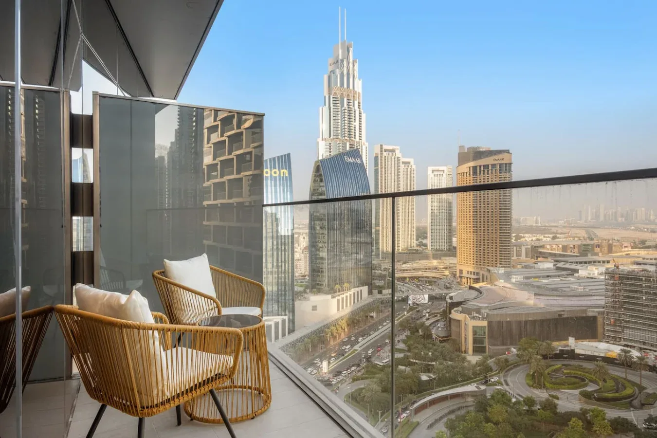 A balcony with woven seating overlooks a city skyline and landscaped roads.