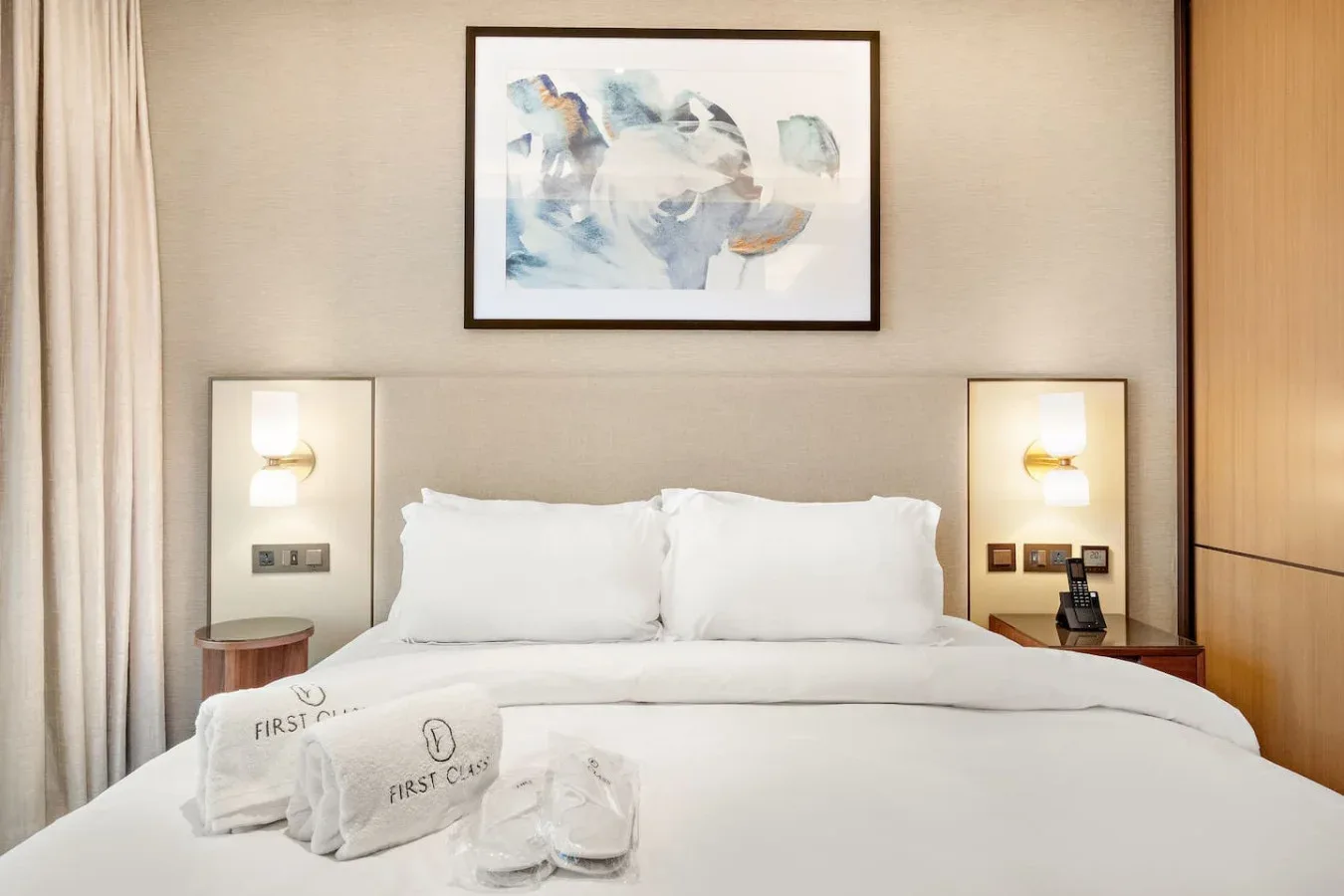A neatly made bedroom features white bedding and framed artwork above the bed.