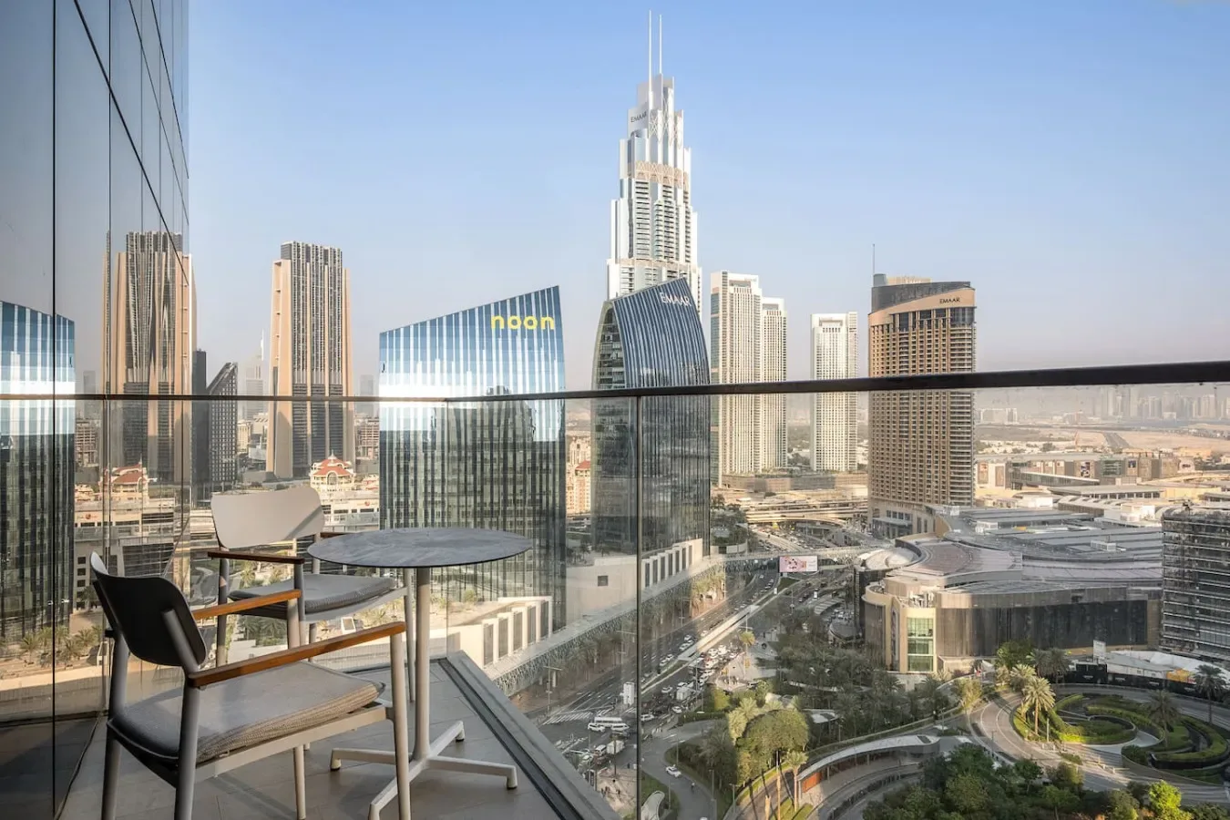 A balcony seating area overlooks a city skyline through a glass railing.