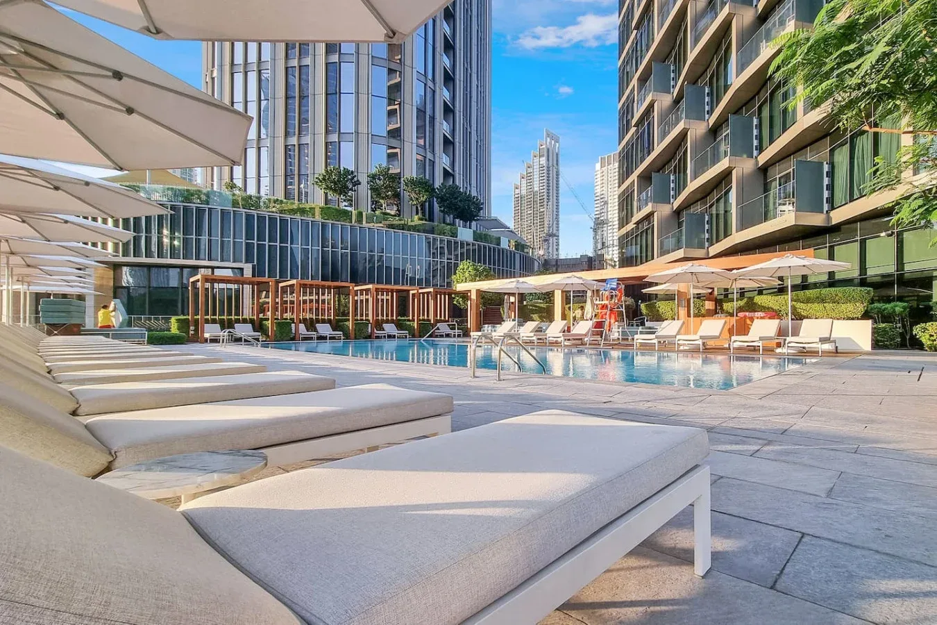 An outdoor pool beside a paved deck with lounge seating and umbrellas.