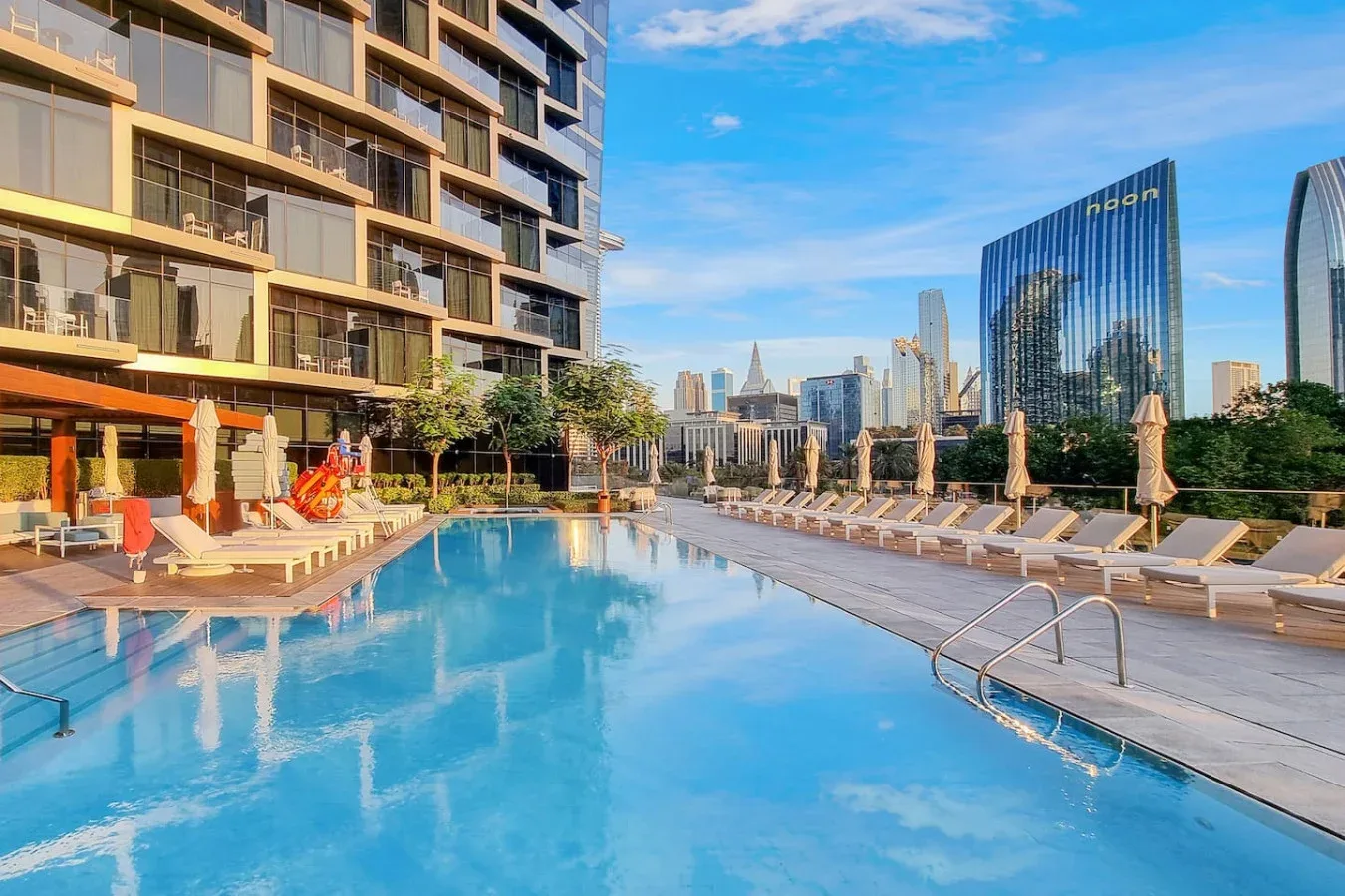 A rooftop pool with lounge seating overlooks a city skyline.