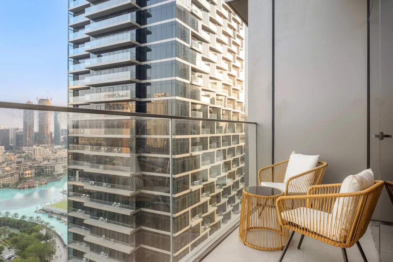 A balcony with woven seating overlooks modern high-rise buildings and a waterfront.