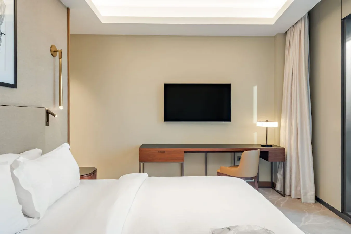 A bedroom with a bed, wall-mounted television, and desk.