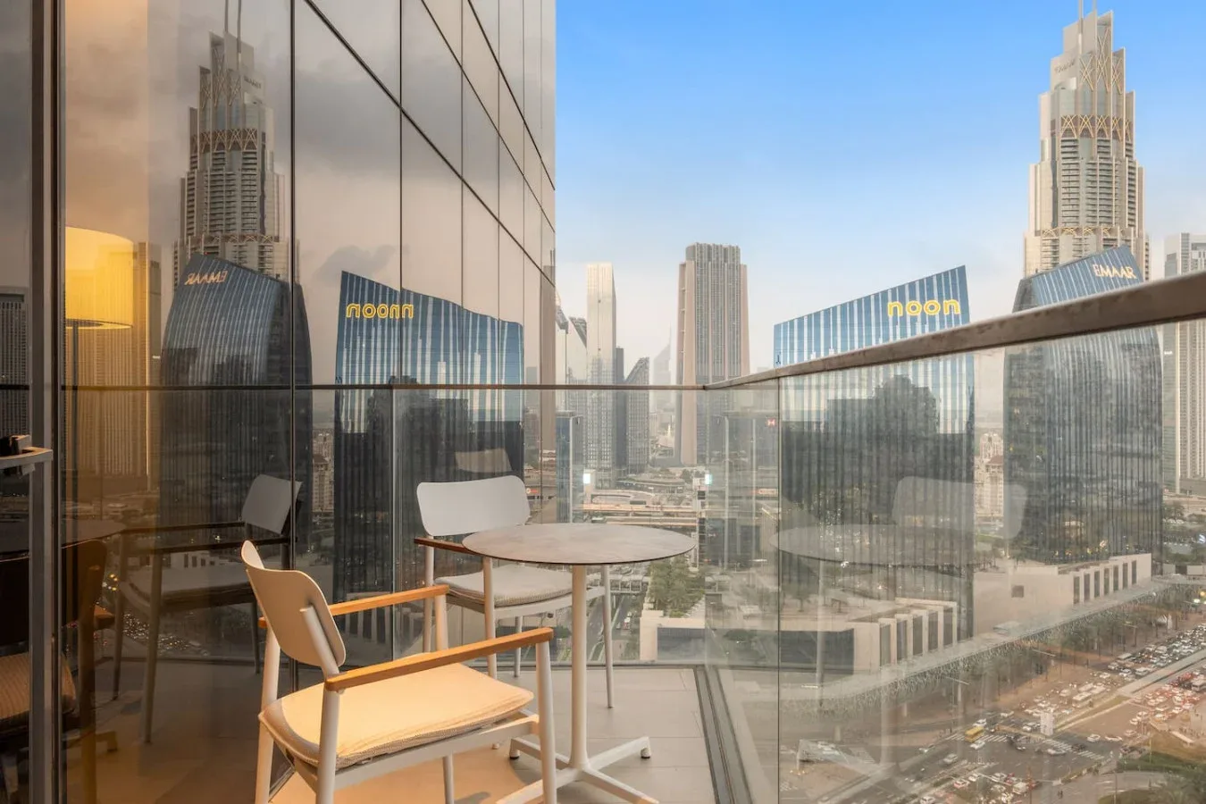 A balcony seating area overlooks a city skyline through glass railings.
