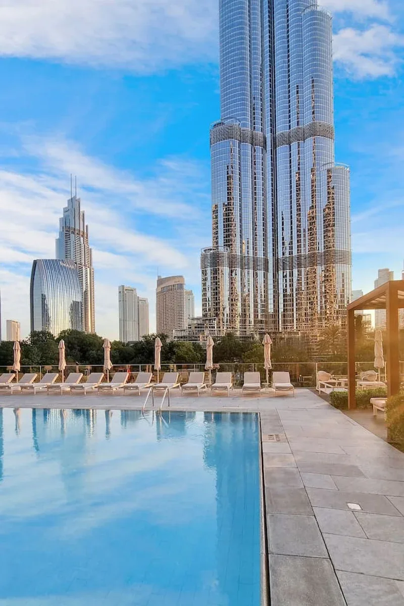 A rooftop swimming pool overlooks a city skyline, with a tall glass tower in view.