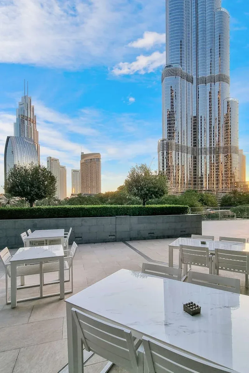An outdoor terrace with tables and seating overlooks a city skyline.